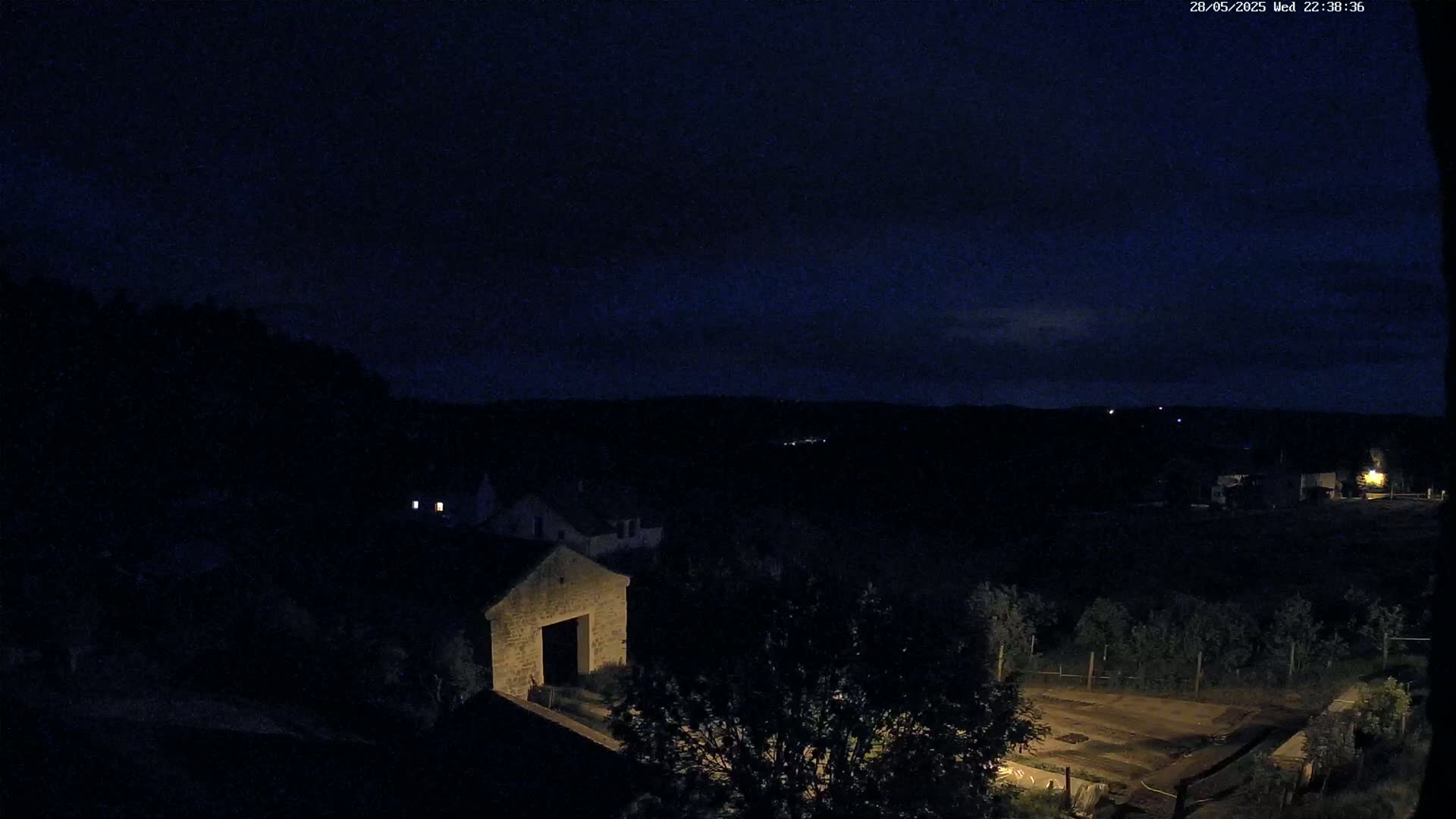 A nighttime, high-angle view shows a stone building and surrounding dark landscape under a mostly clear, dark blue sky.