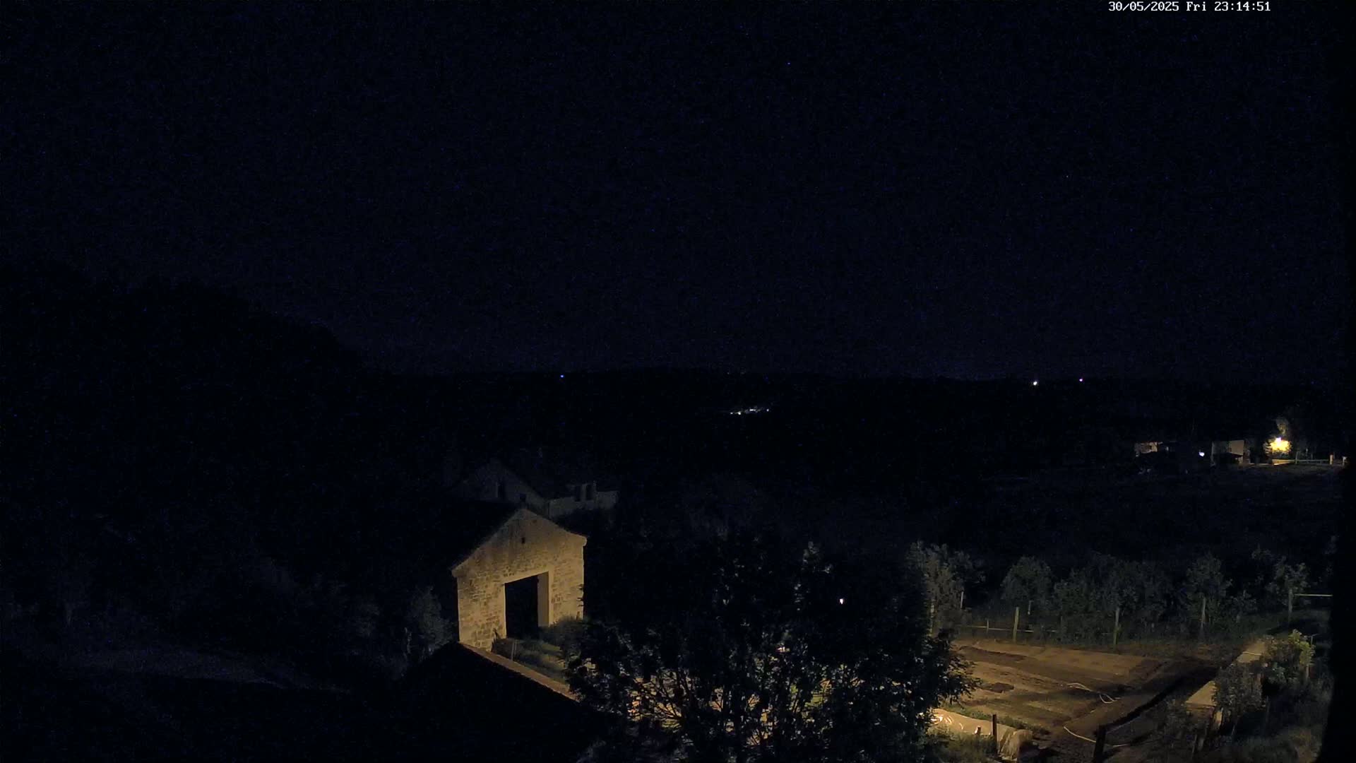 A nighttime view shows a stone building and some trees under a clear, dark sky.