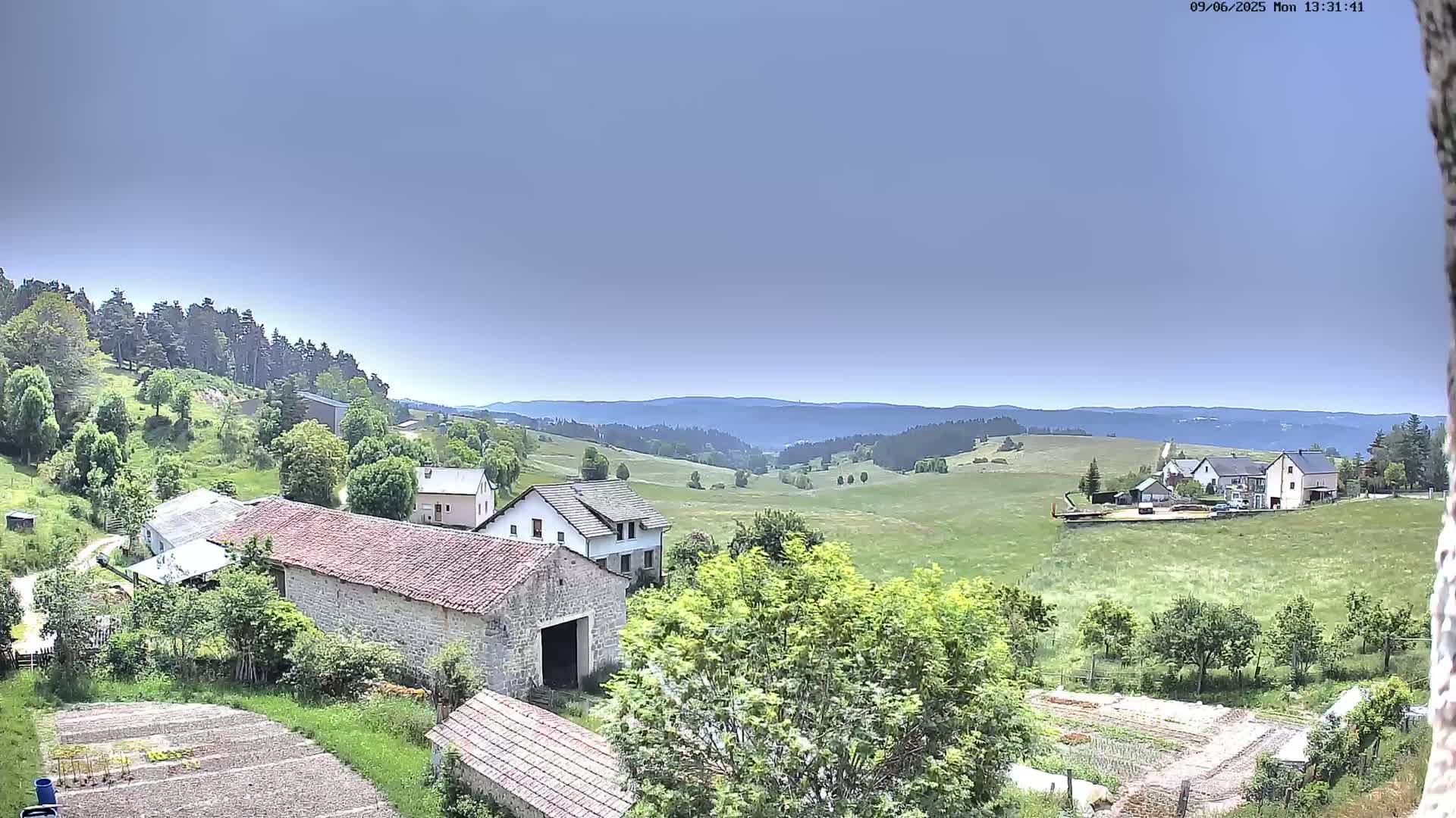 A sprawling landscape of green fields and stone buildings under a clear, light-blue sky.