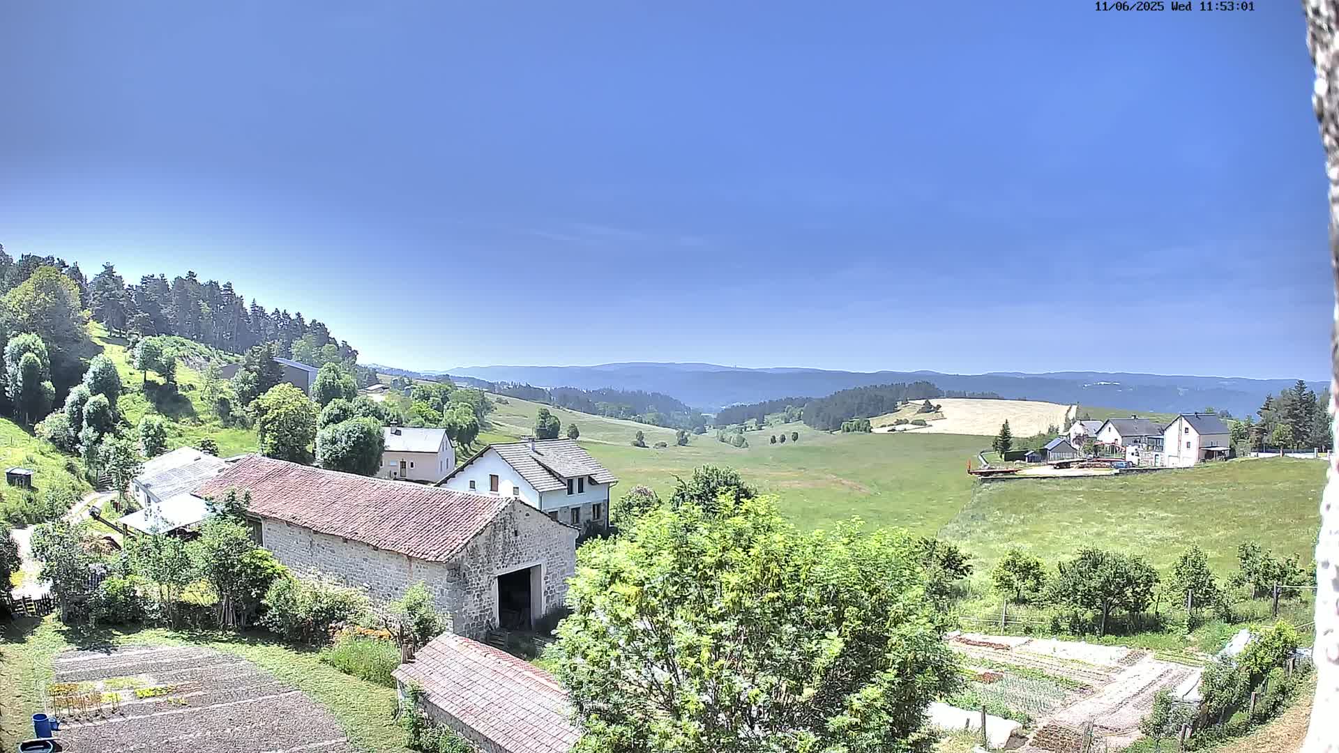 A sprawling green valley dotted with farmhouses and gardens under a clear blue sky.