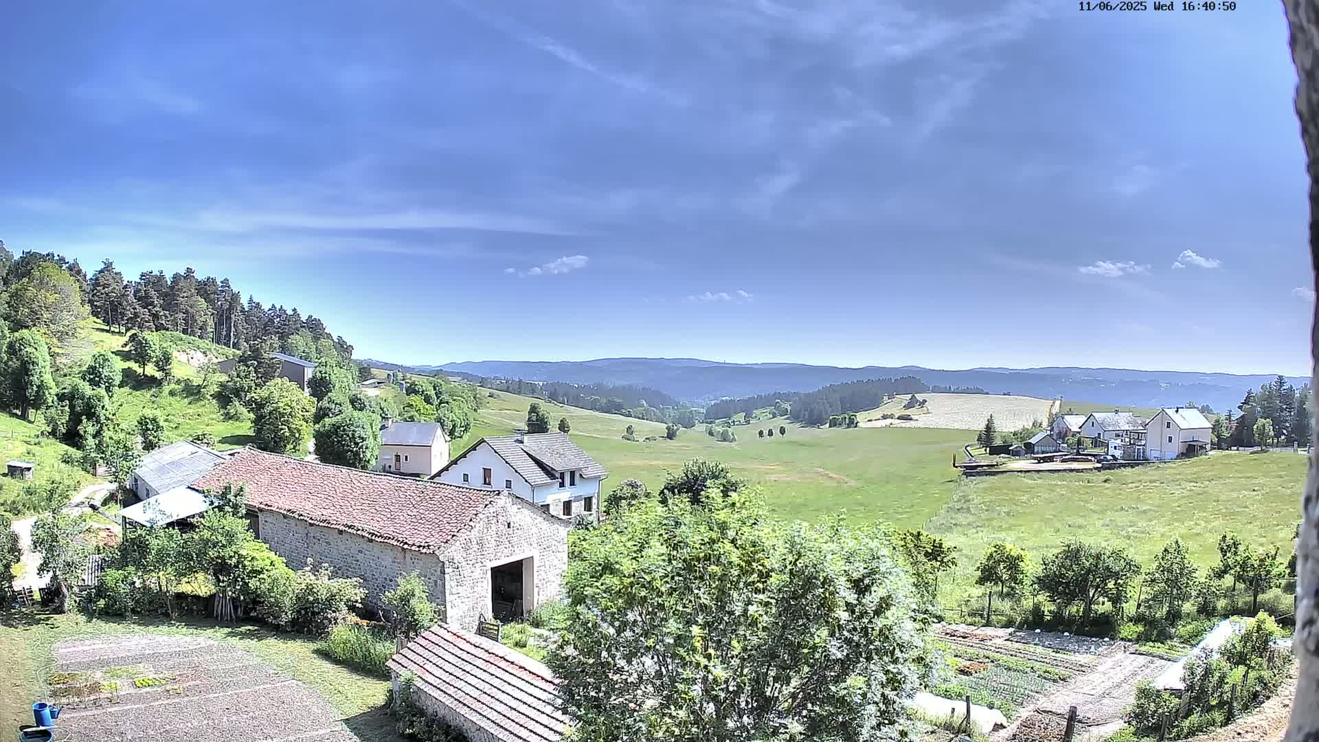 A mostly sunny day overlooking a rural landscape of farmhouses, green fields, and forests in a valley.