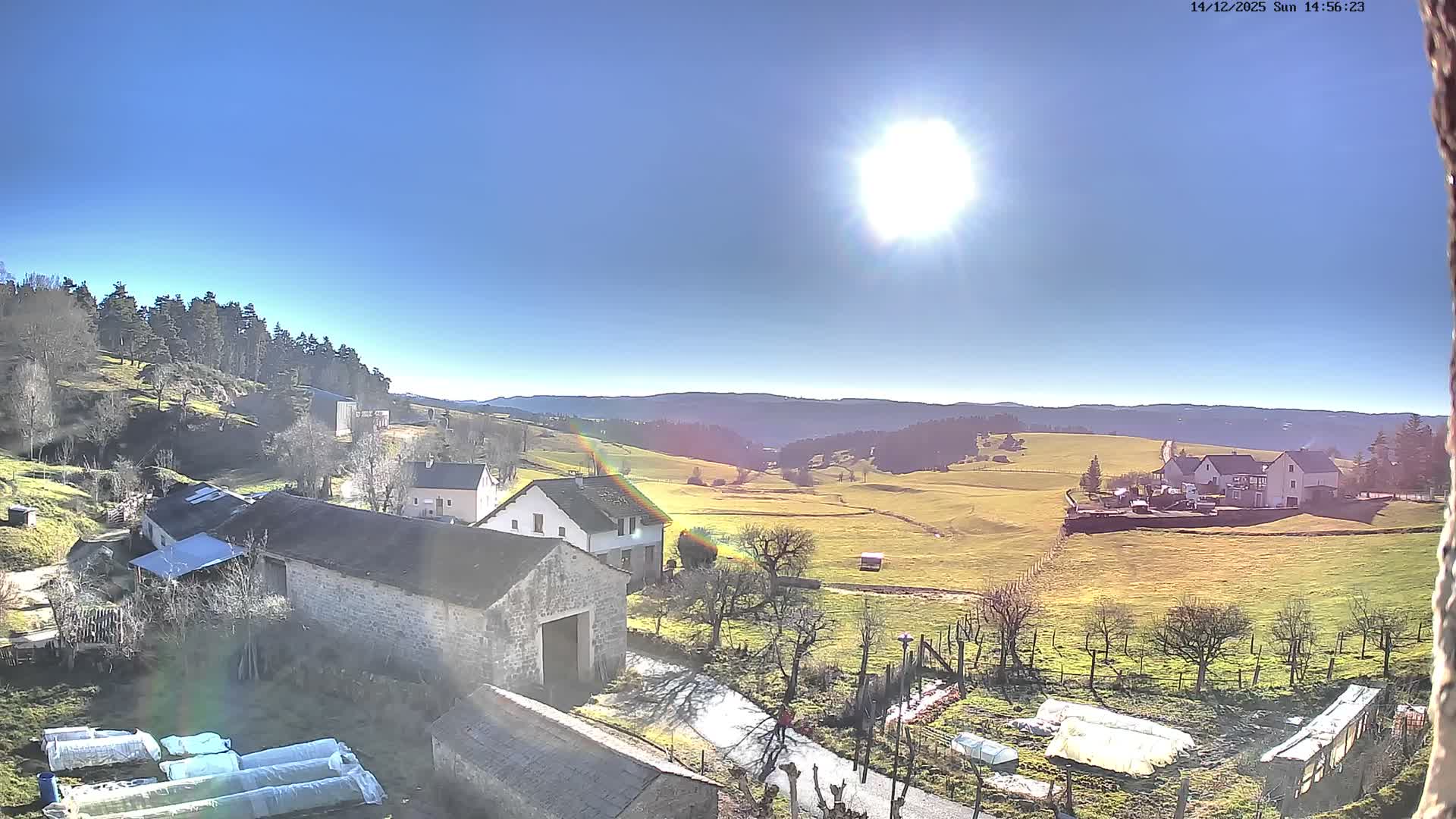 A panoramic view reveals a rural landscape entirely blanketed in fresh snow, with scattered houses, snow-laden trees, and gentle hills fading into a uniformly grey, overcast sky on a cold winter day.