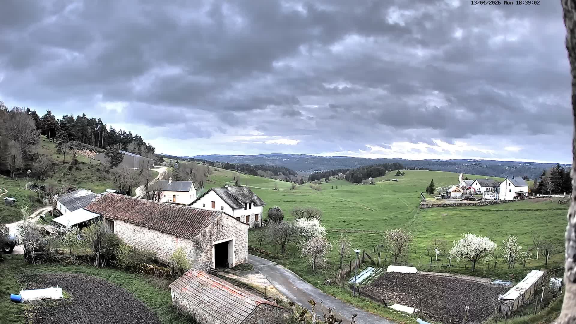 A panoramic view reveals a rural landscape entirely blanketed in fresh snow, with scattered houses, snow-laden trees, and gentle hills fading into a uniformly grey, overcast sky on a cold winter day.