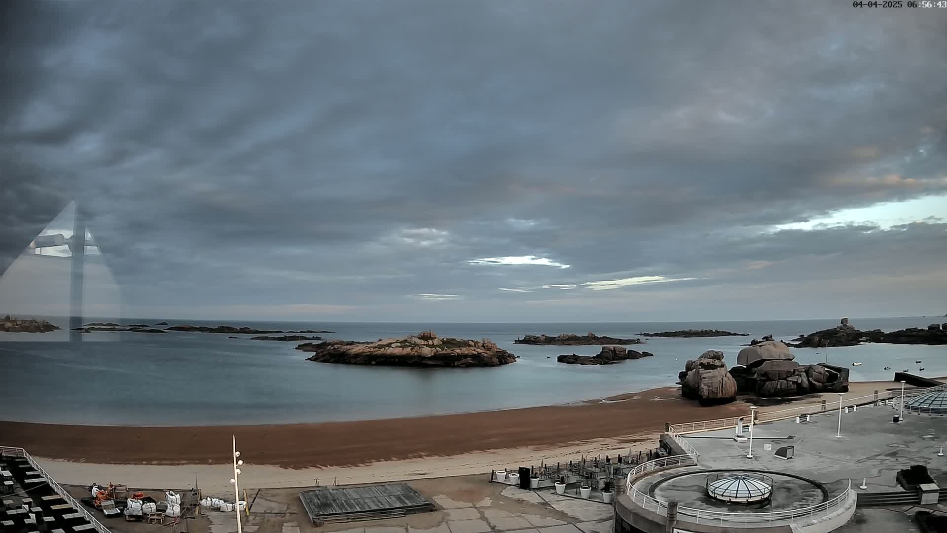 A sandy beach with rocky islands in a calm sea under a cloudy sky.