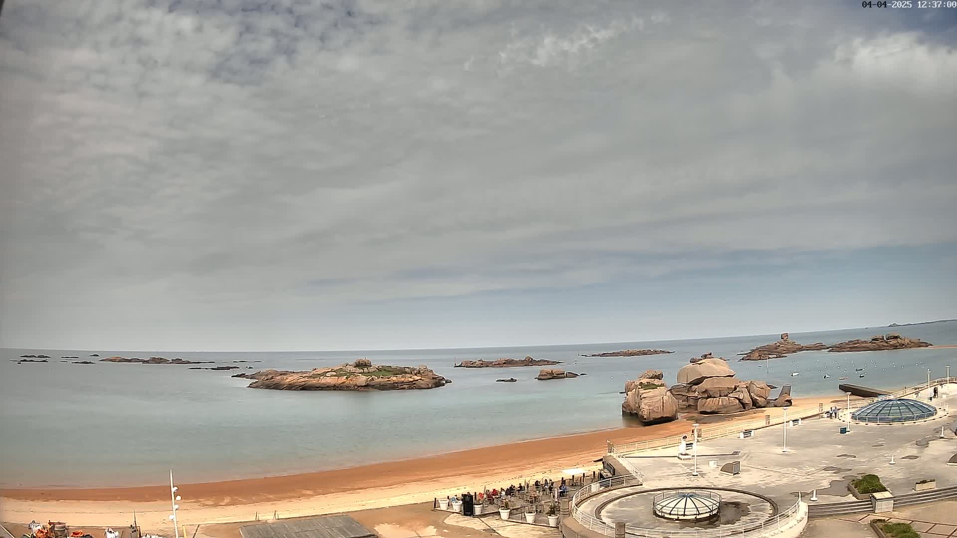 A sandy beach with rocky outcrops in a calm sea under a mostly cloudy sky.