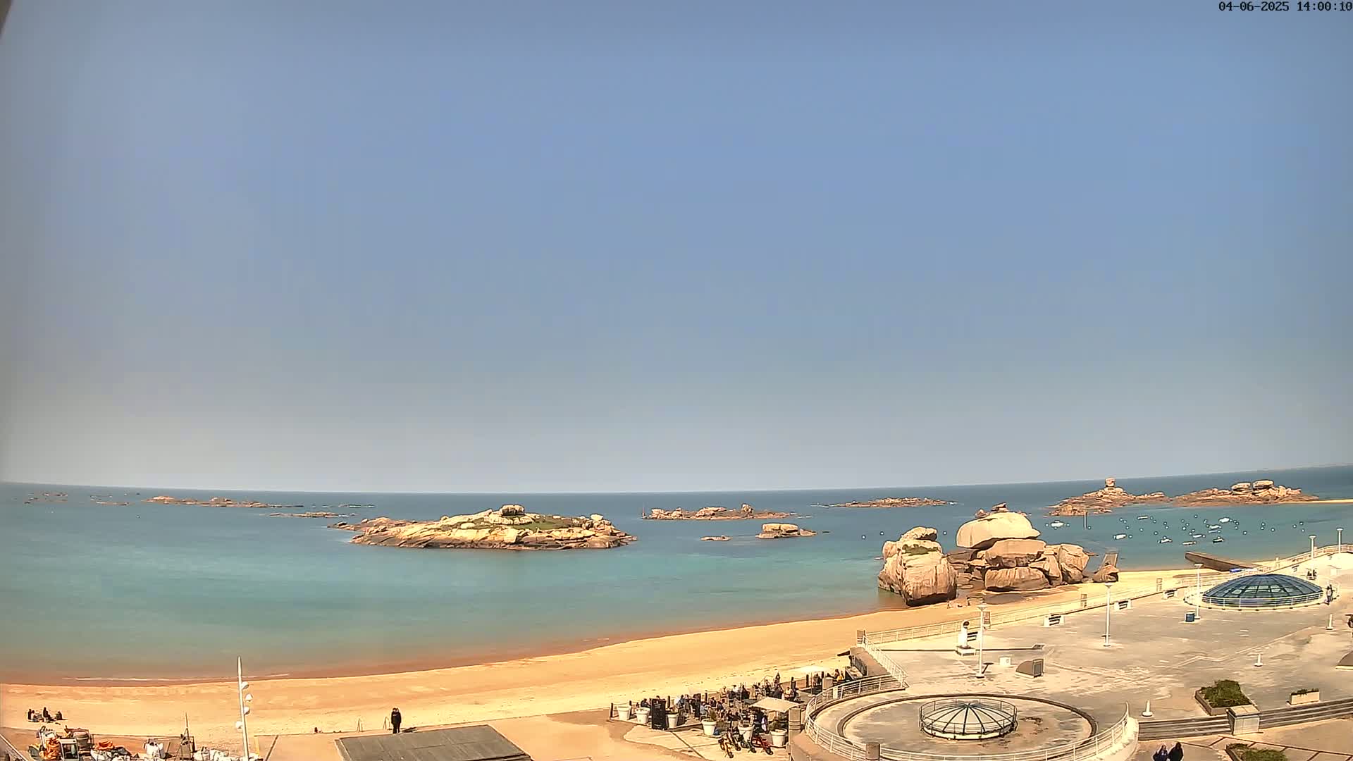 A sandy beach with rocky outcroppings in a calm, clear ocean under a bright, sunny sky.
