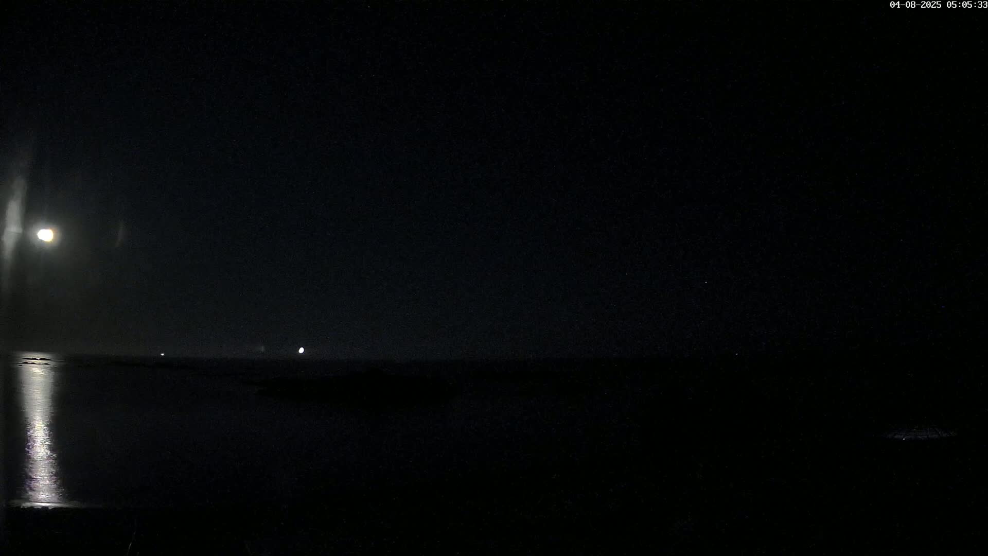 A bright moon illuminates a dark, calm body of water at night.
