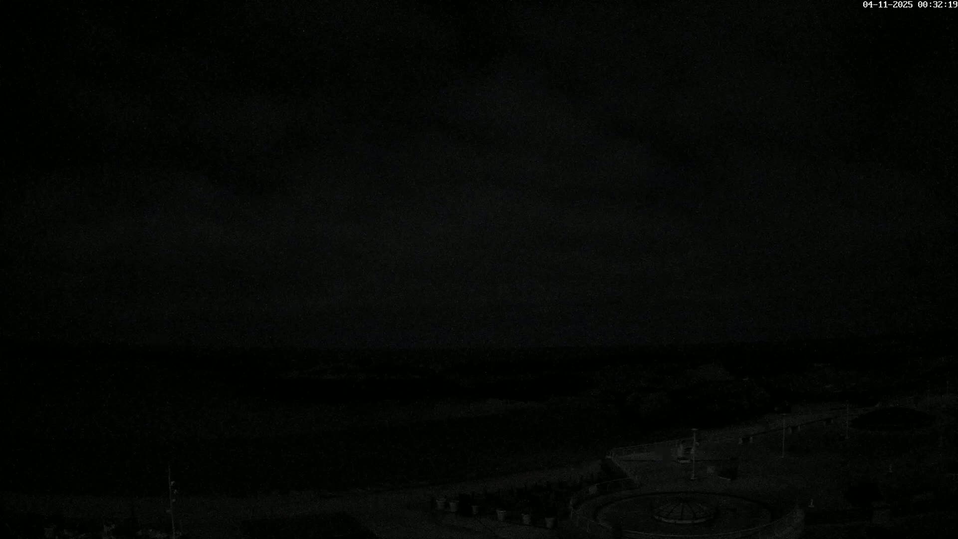 A dark, nighttime outdoor scene shows a mostly obscured landscape with a circular feature and some lights visible near the bottom.