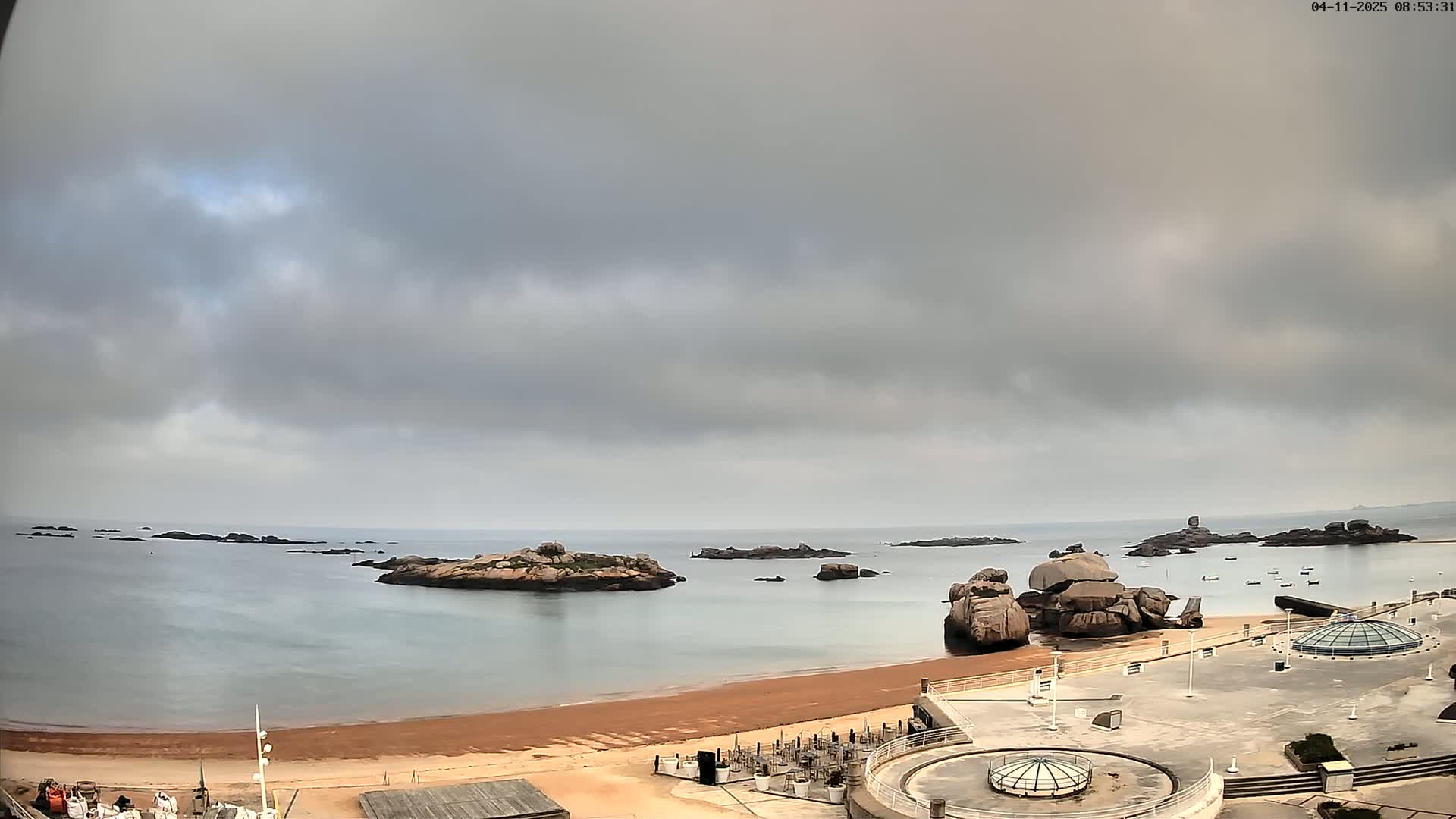 A sandy beach with several large rocks in the water under an overcast sky.