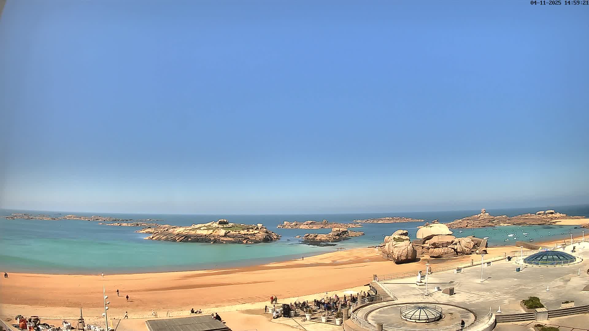 A sandy beach with turquoise water and rocky outcrops is seen under a clear blue sky.