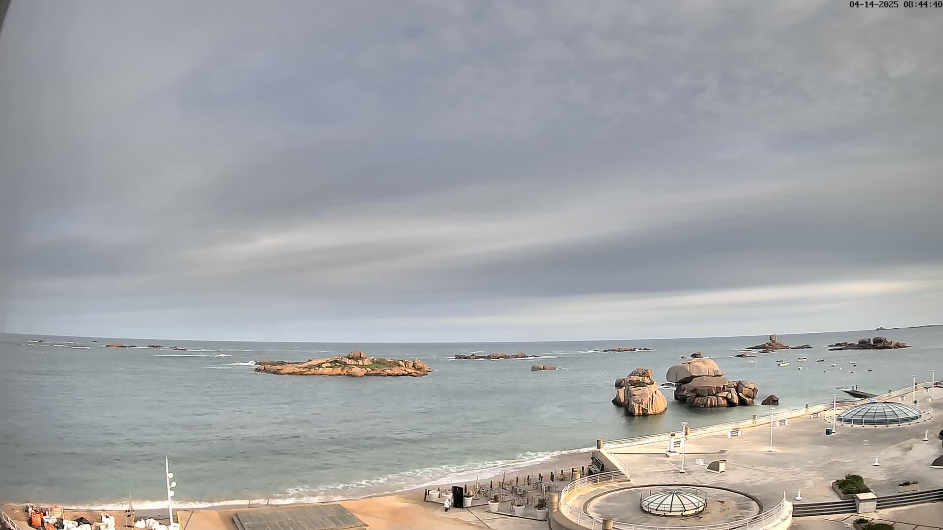 A beach with rocky outcrops in a calm sea under a cloudy sky.