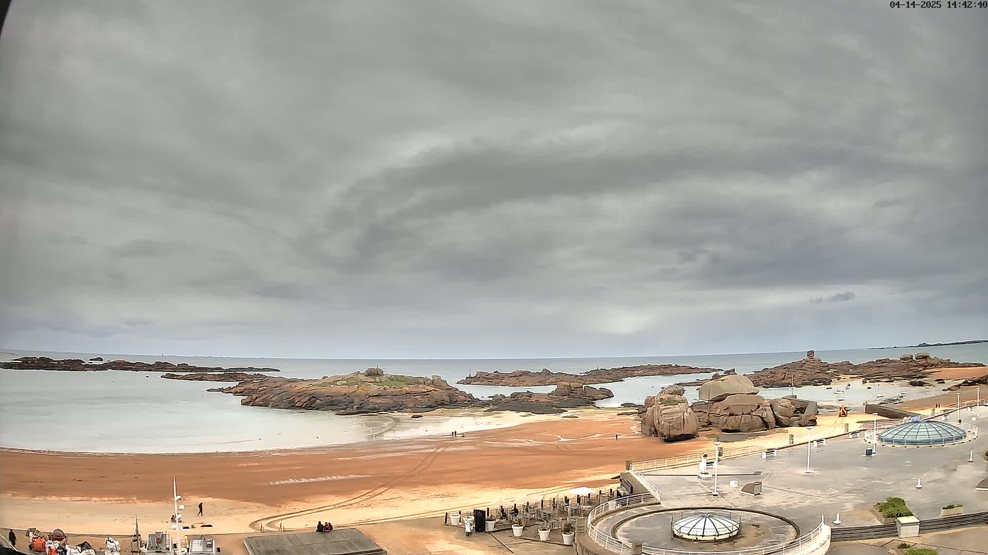 A sandy beach with rocky outcrops and calm water is viewed under an overcast sky.