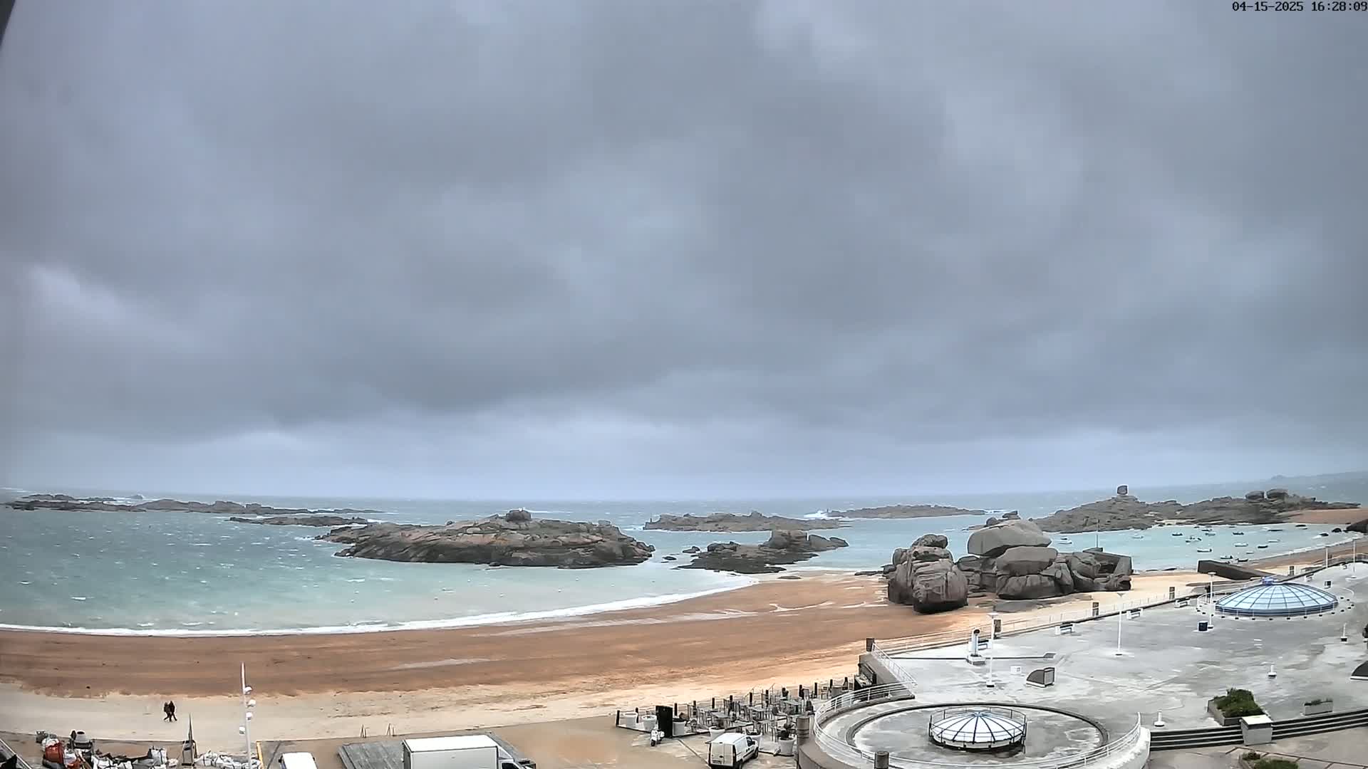 A windy, overcast day reveals a sandy beach, rocky coastline, and calm, choppy water.