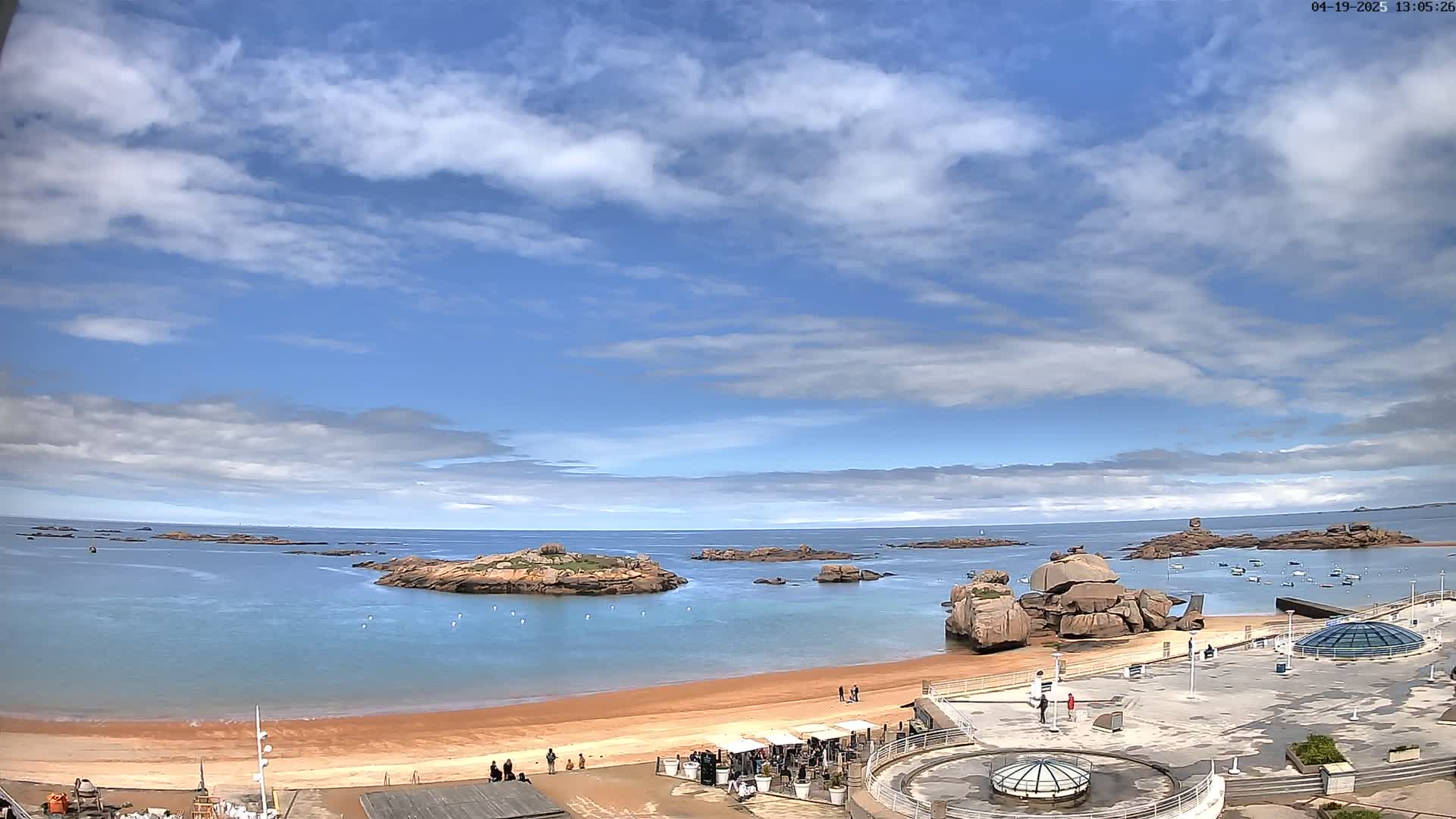 A sandy beach with rocky outcrops in a calm, blue ocean under a partly cloudy sky.