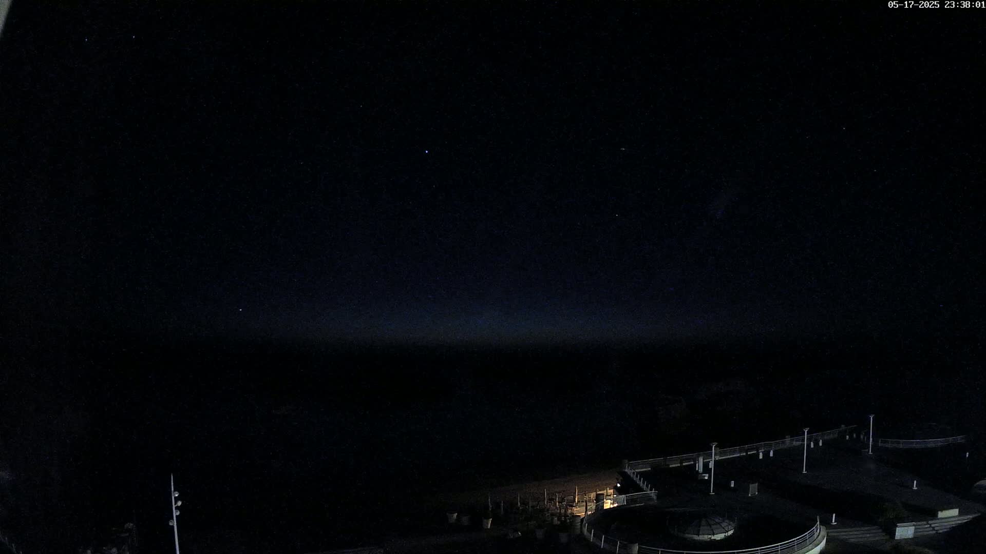 A nighttime view shows a dark body of water under a clear, starlit sky, with a dimly lit pier and surrounding structures visible in the foreground.