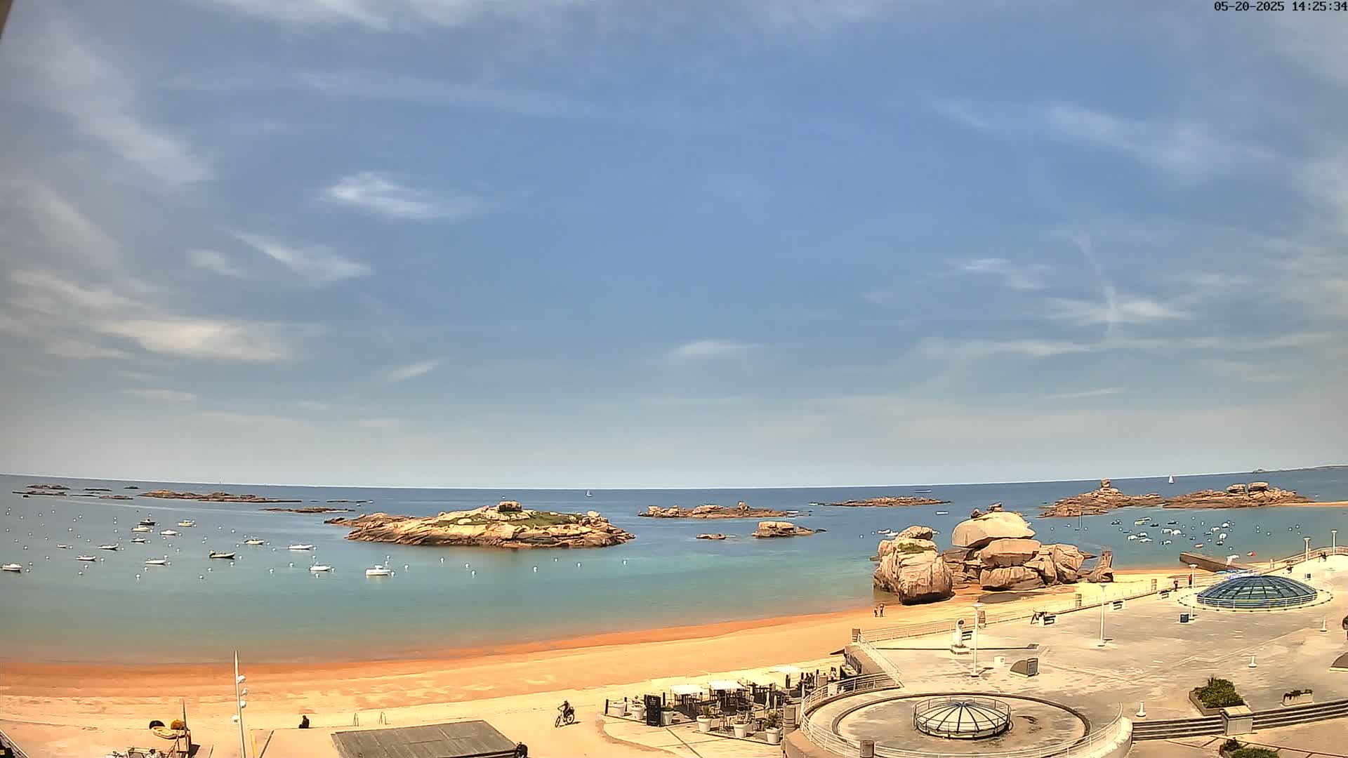 A sandy beach with calm, light-blue water and several rocky islands under a mostly sunny sky with scattered clouds.