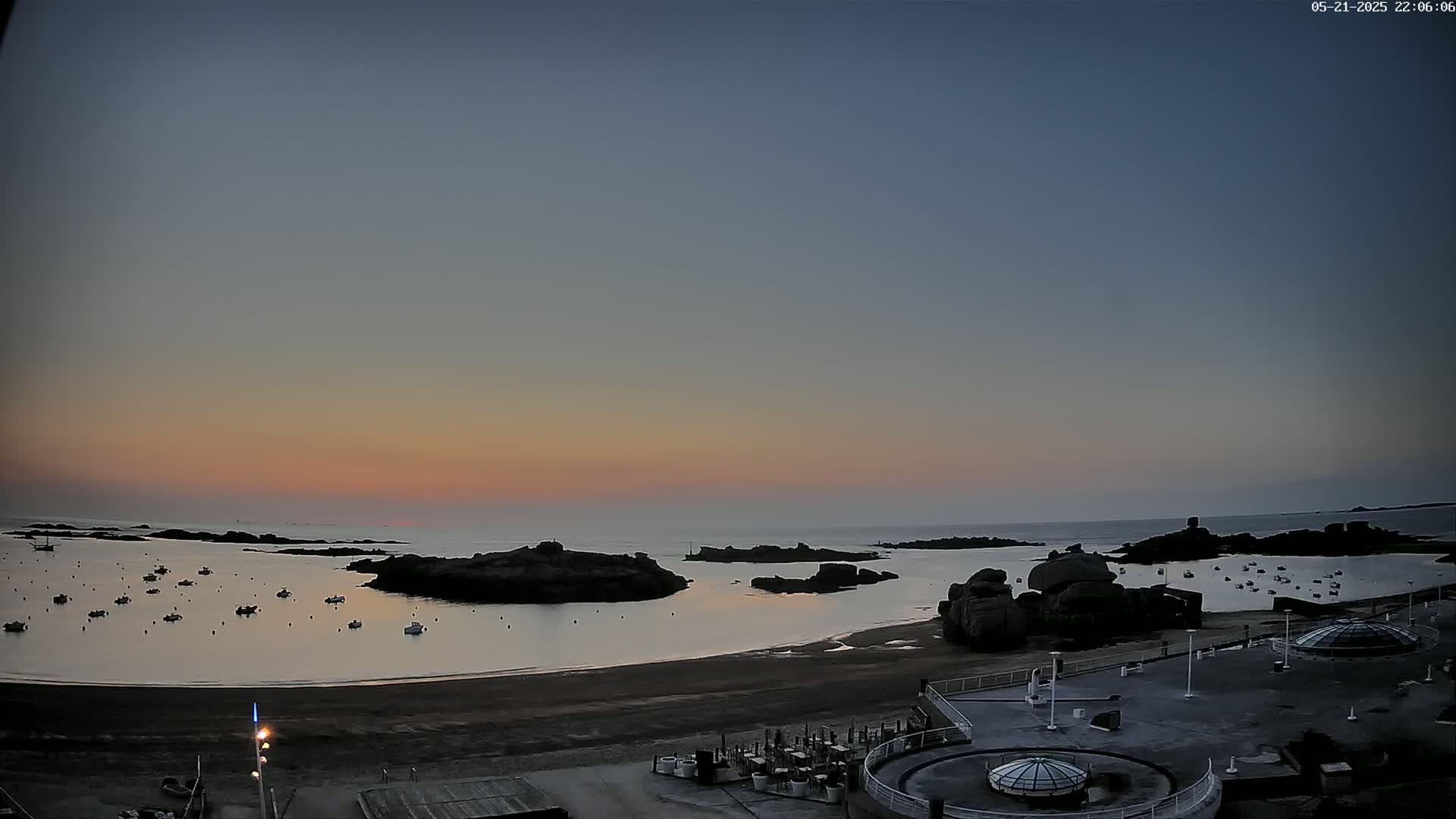 A tranquil sunset over a calm bay with several boats and rocky outcrops, viewed from a high vantage point.