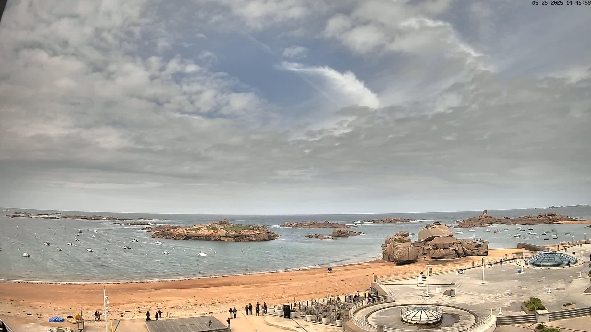 A sandy beach with several small boats in the calm water, rocky outcrops, and overcast skies.