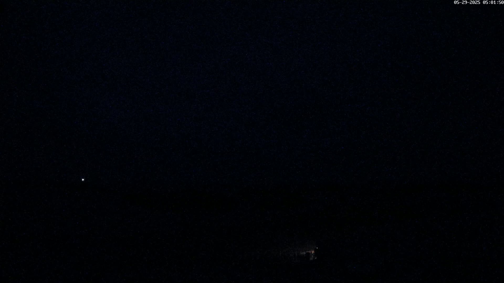 A dark night scene shows a faint light in the distance and a few stars in a mostly clear sky.