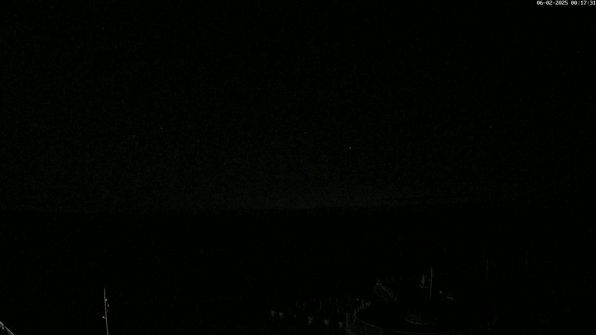 A nighttime, low-light view shows a dark, mostly featureless landscape with a few faint lights in the distance.