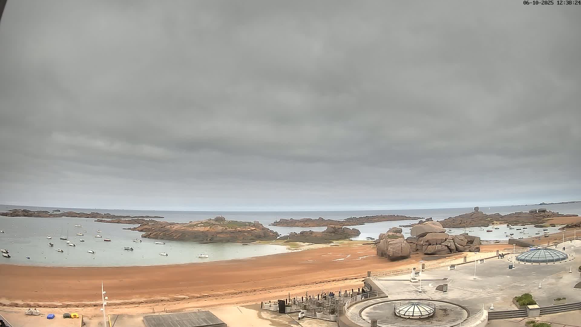 A sandy beach with several boats in a calm bay, surrounded by rocky outcrops under an overcast sky.