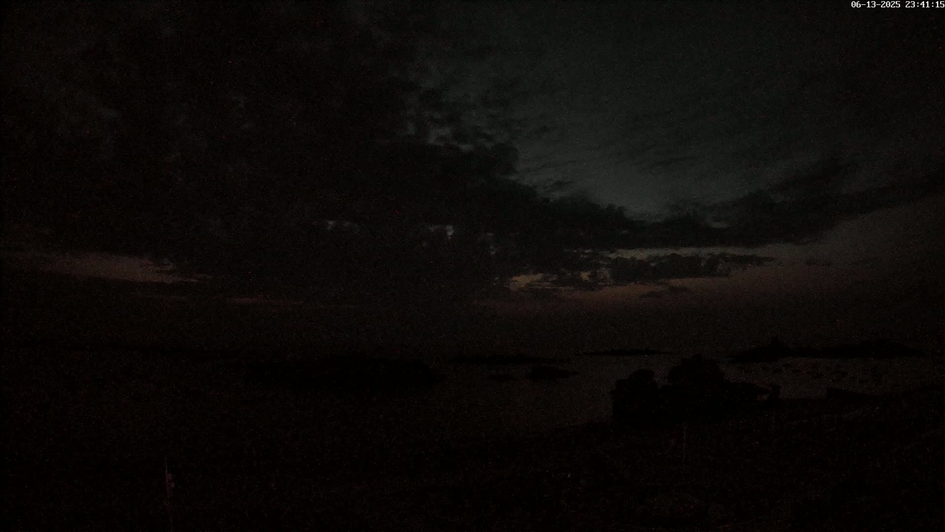 A dark, cloudy night scene shows a body of water with a silhouetted shoreline.