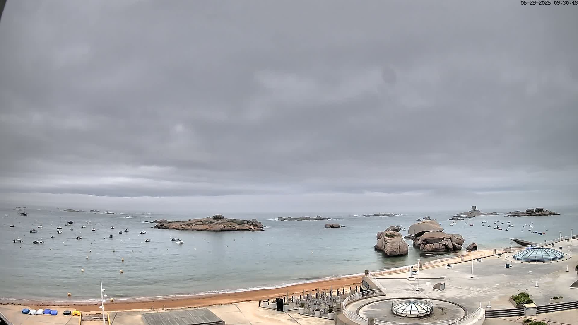 A calm bay with numerous small boats and rocky outcrops under a cloudy sky.