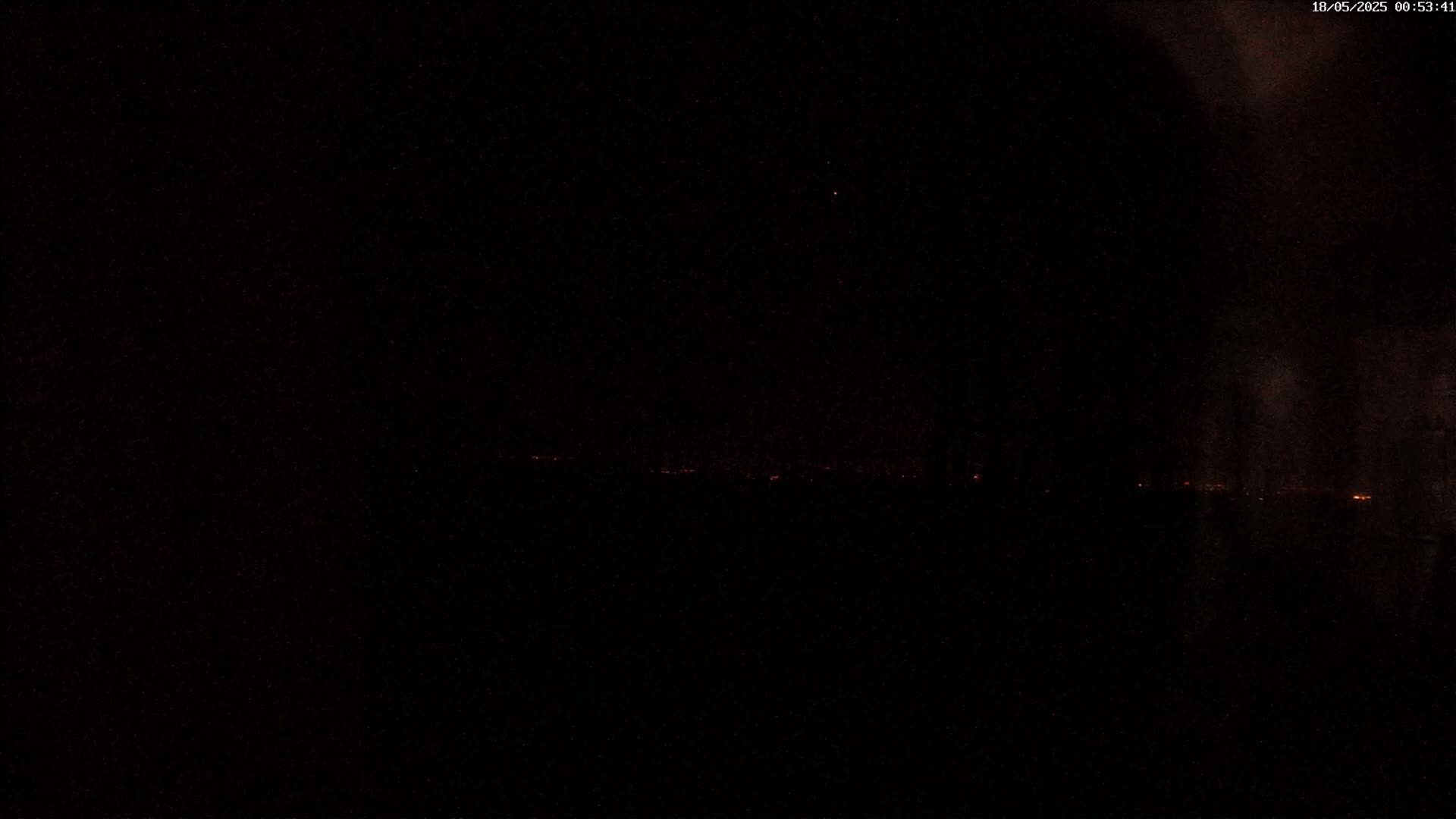 A nighttime long shot shows a faint line of distant lights on the horizon under a dark, clear sky.