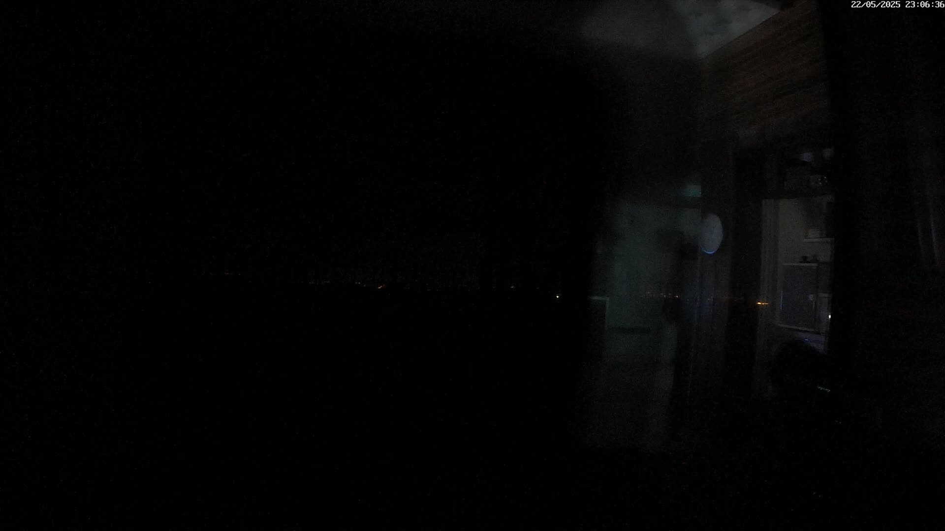 A dark, nighttime interior scene shows a dimly lit room and a view of a distant, faintly lit landscape through a window.