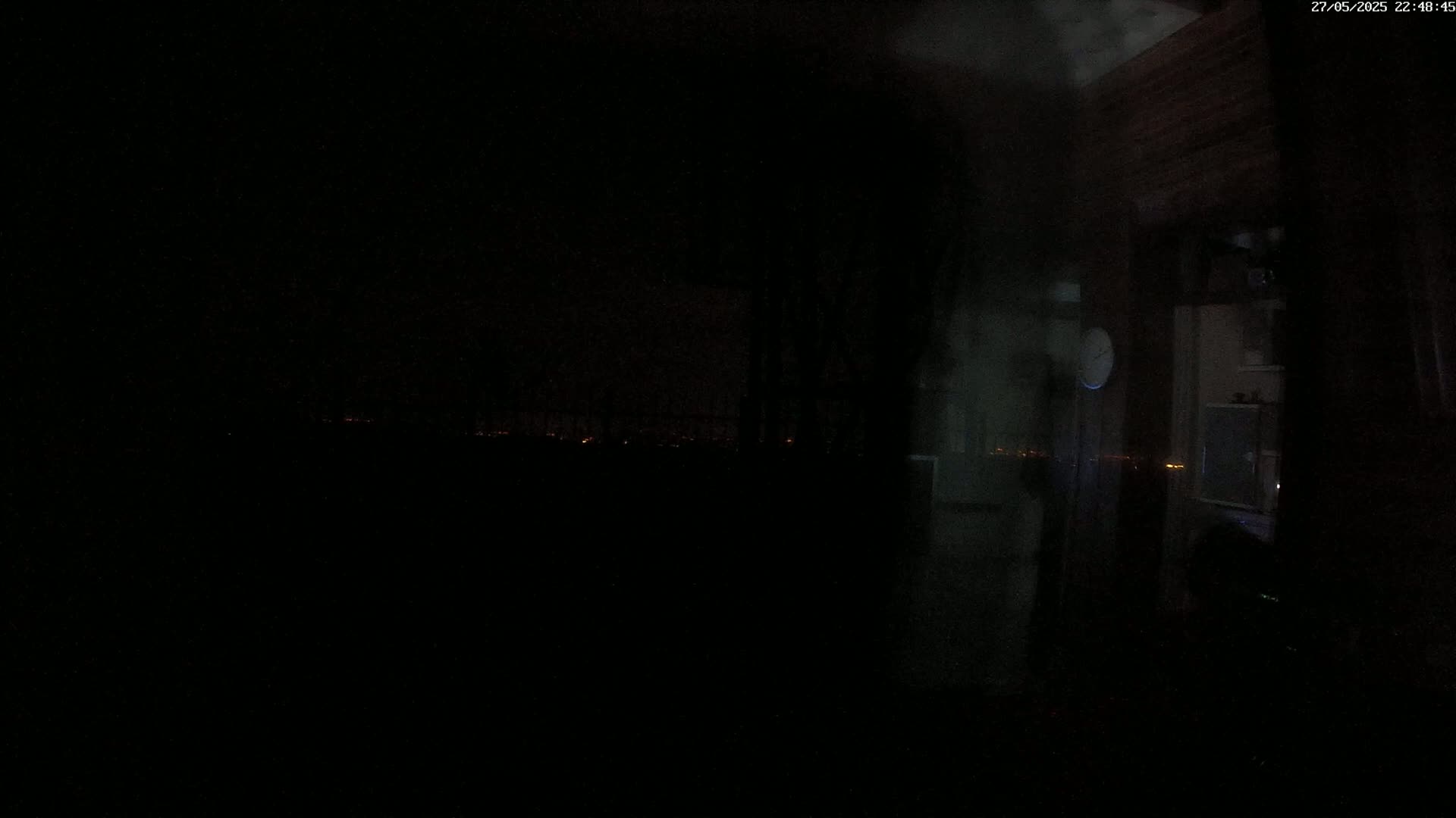 A dark, nighttime interior view shows a blurry, dimly lit room and a distant, faint cityscape through a window.