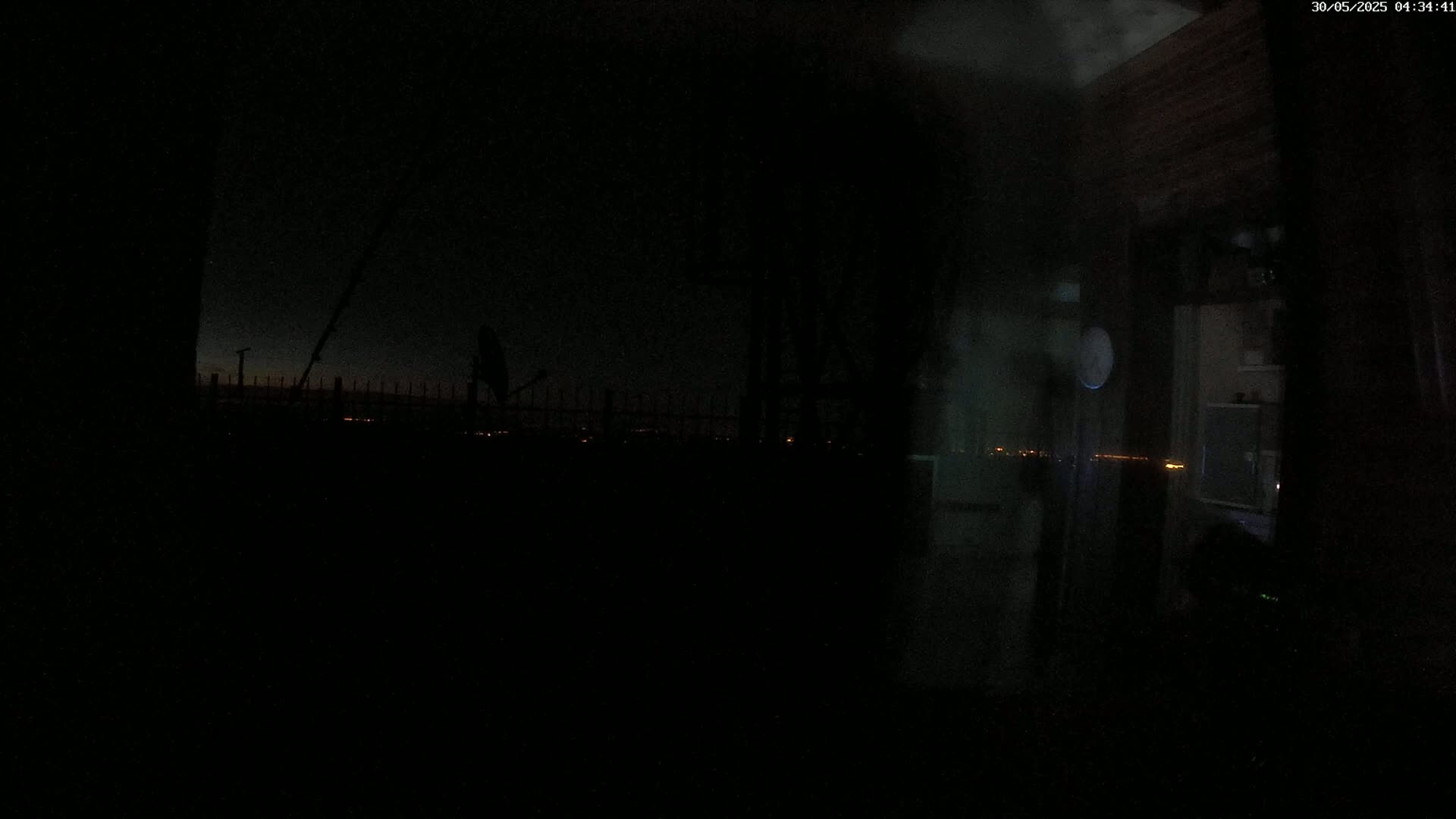 A nighttime view from inside a building shows a dark, mostly obscured outdoor scene with a distant city skyline illuminated by faint lights.