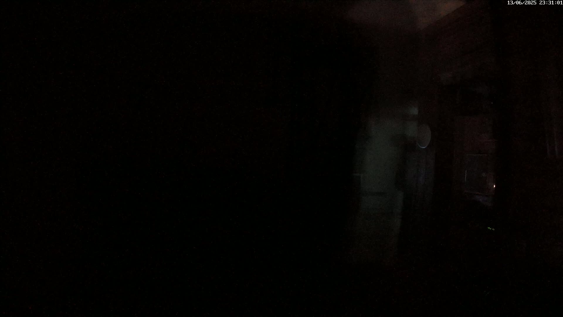 A very dark interior scene is visible, with only a small portion of the room illuminated, showing indistinct shapes and a possible reflection.