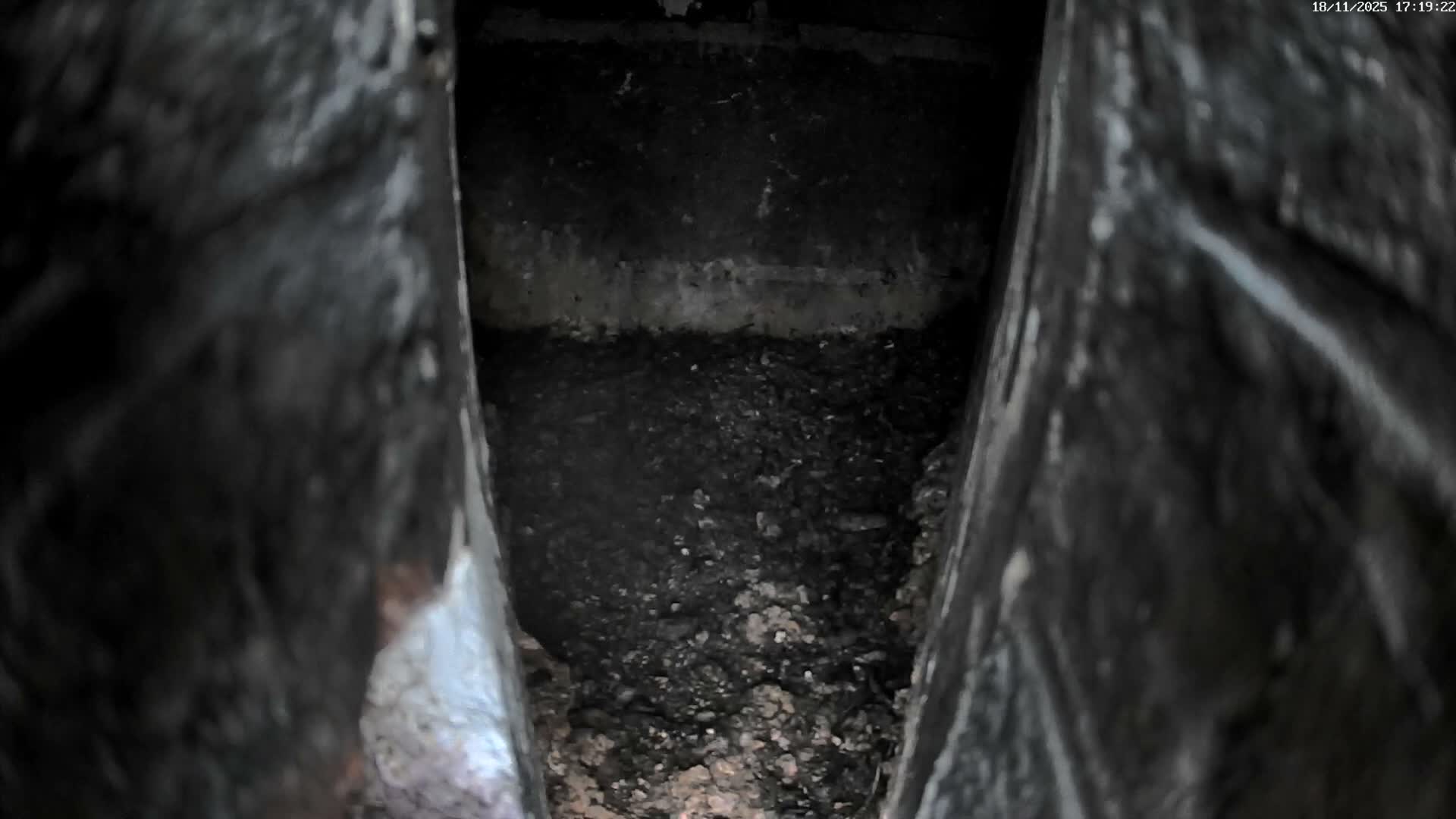 A narrow, dark cavity reveals a pile of dark brown dirt and debris.