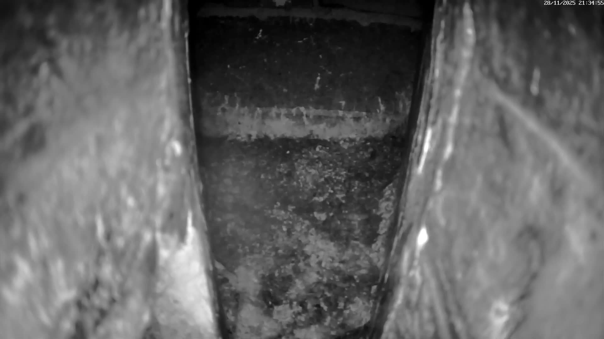 A grayscale image depicts the interior of a narrow, textured crevice or pipe, revealing a rough, granular surface at the bottom and a lighter horizontal band on the back wall.