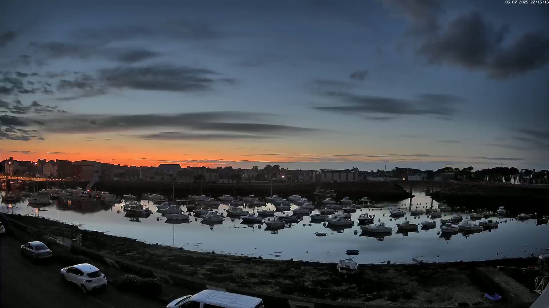 Numerous small boats are moored in a calm harbor at sunset under a partly cloudy sky.