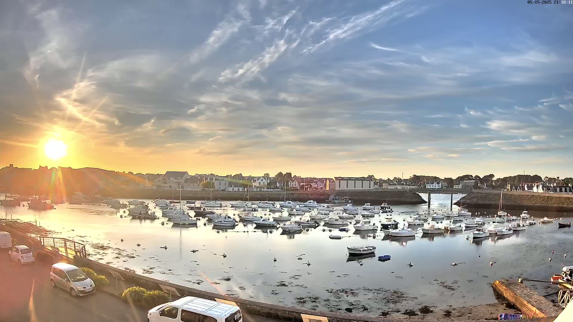Many white boats are moored in a calm harbor at sunset under a partly cloudy sky.