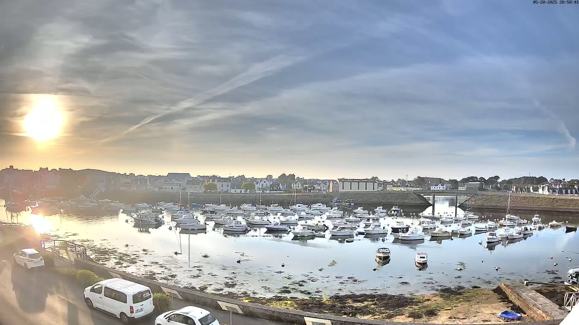 A calm harbor filled with numerous small boats at sunset under a partly cloudy sky.