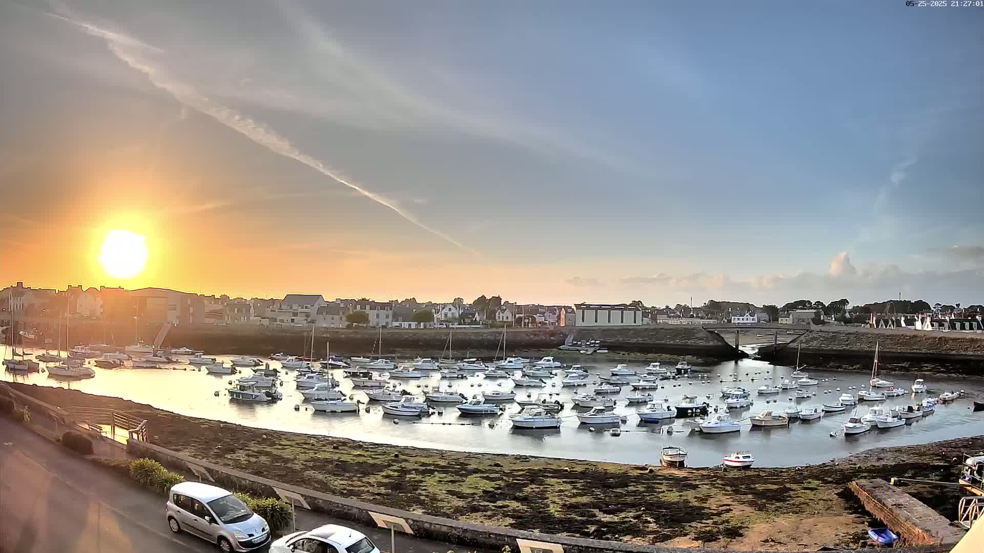 Many boats are moored in a harbor at sunset under a mostly clear sky.