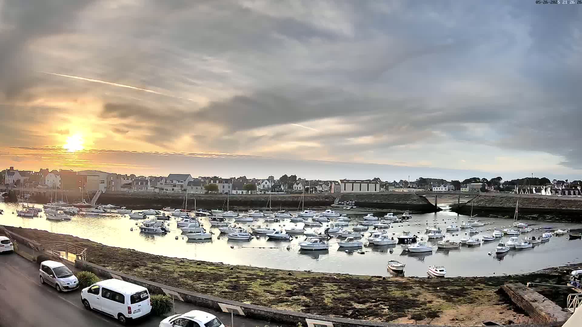 A harbor filled with numerous small boats sits under a partly cloudy sunset sky.
