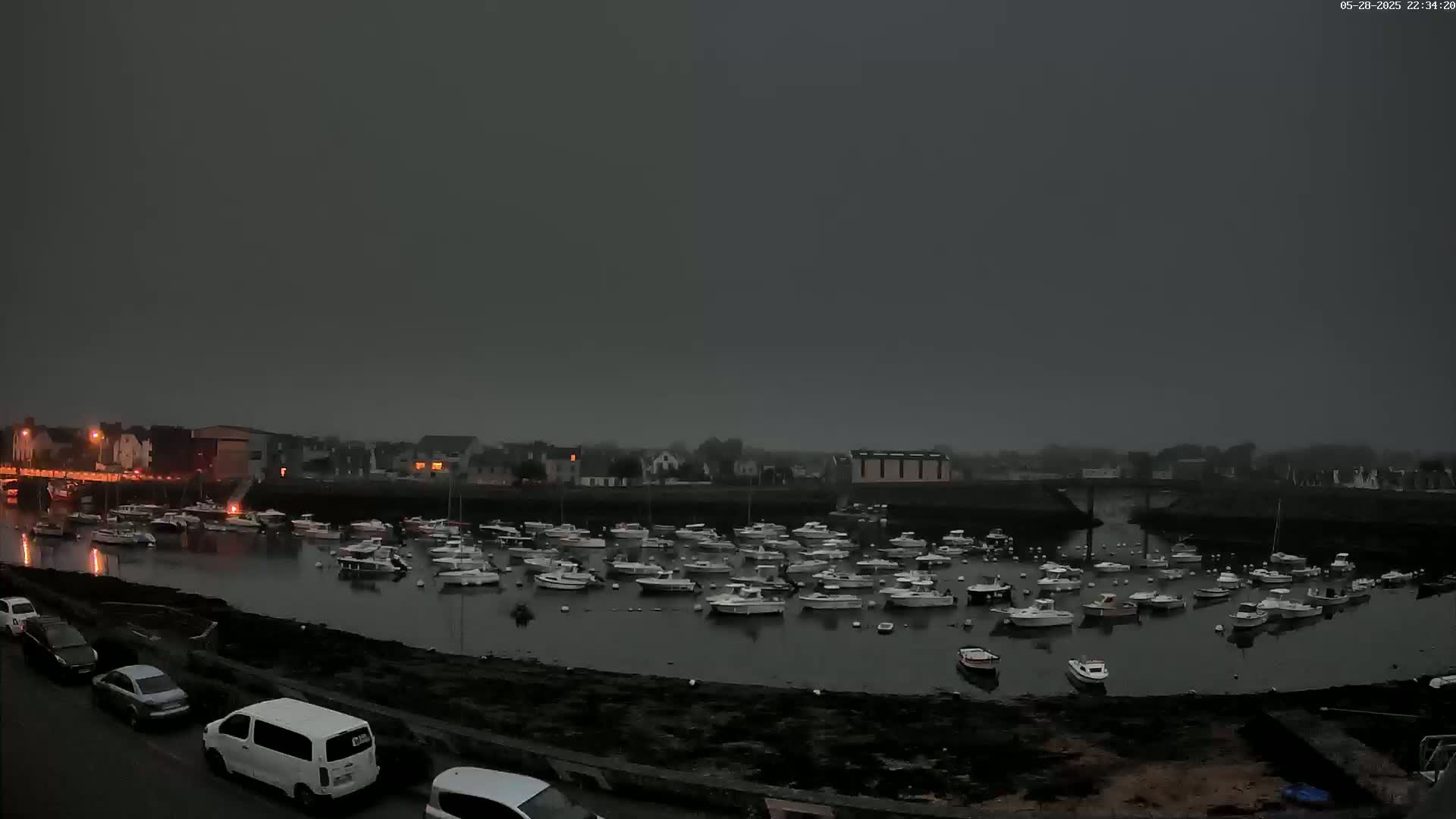 Many small boats are moored in a harbor at dusk under a dark, overcast sky.