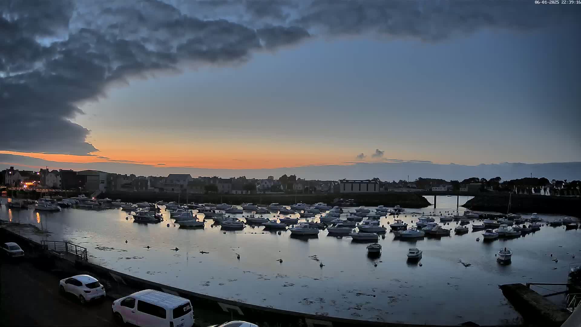 Many boats are moored in a calm harbor at sunset under a partly cloudy sky.