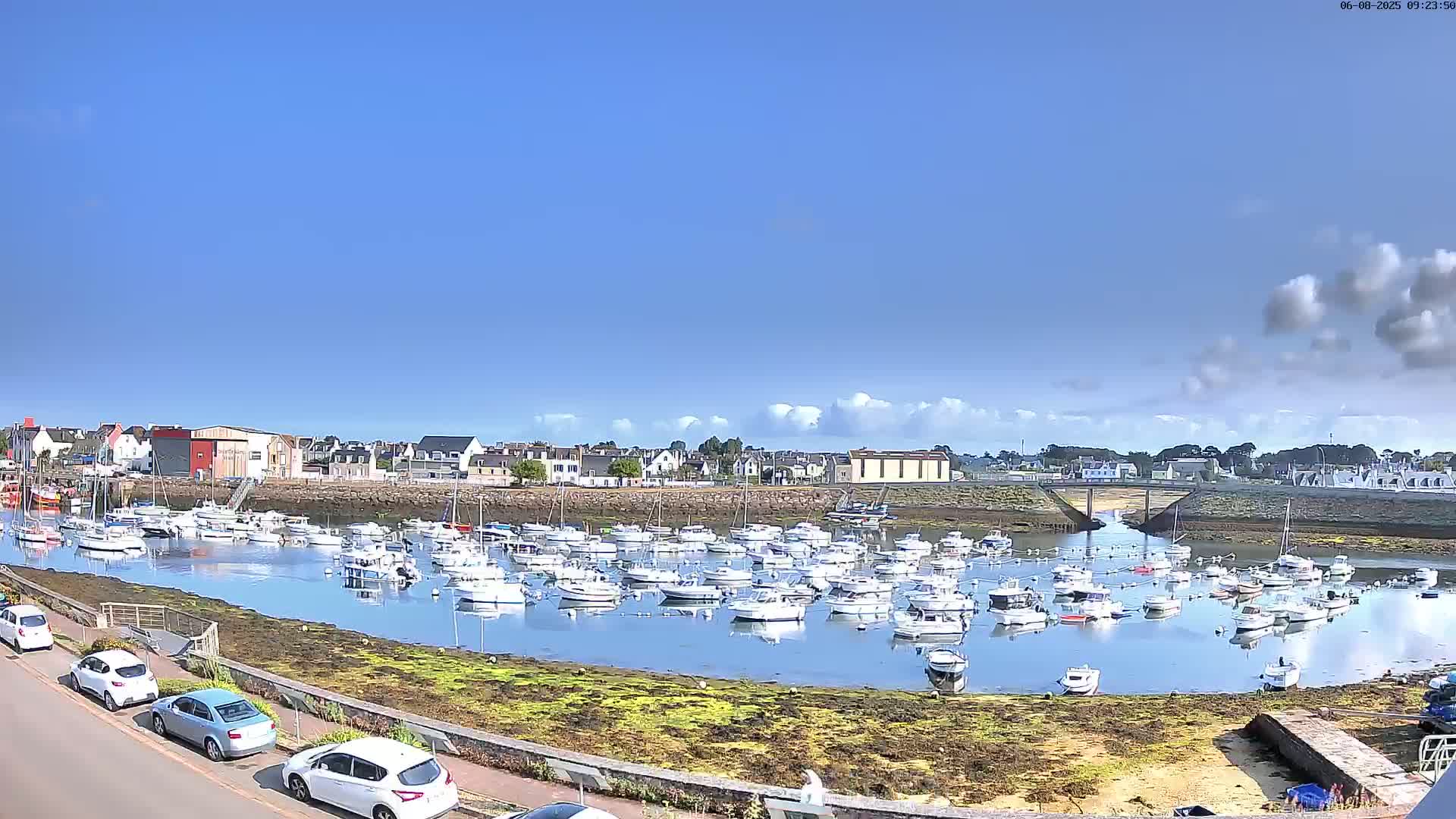 A marina filled with numerous boats is situated in a town on a sunny day with partly cloudy skies.