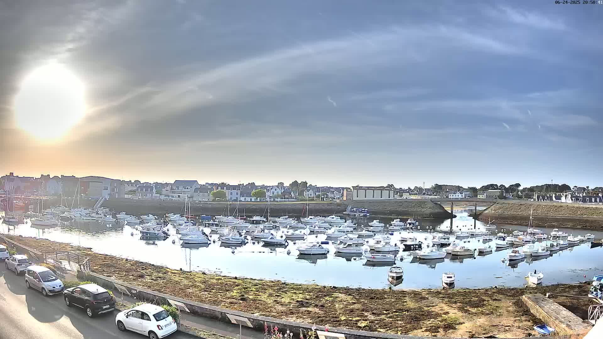 A harbor filled with numerous small boats is seen under a partly sunny sky with thin clouds.