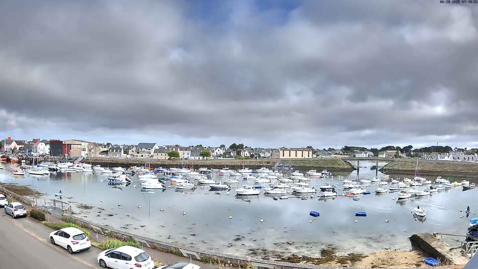 A harbor filled with numerous small boats is situated under a mostly cloudy sky.