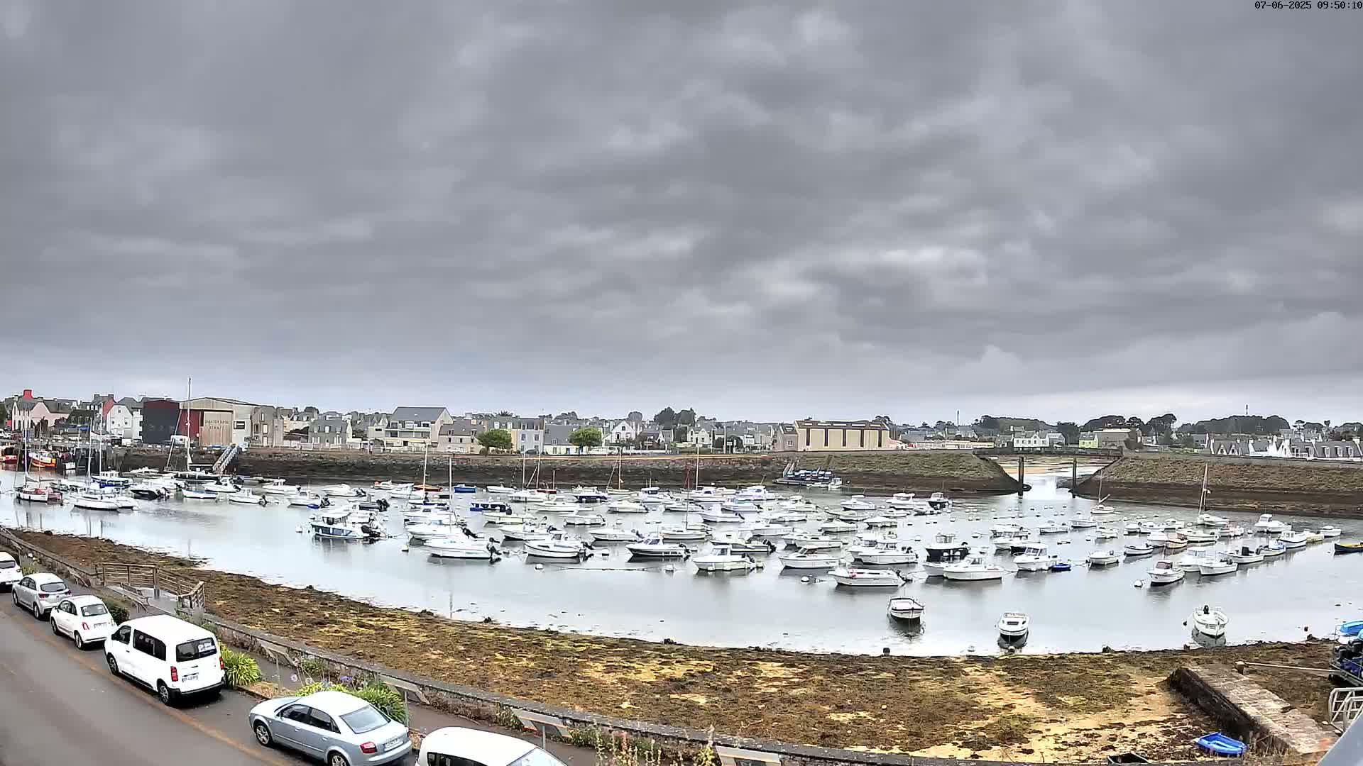 A harbor filled with numerous small boats is situated under a cloudy sky.