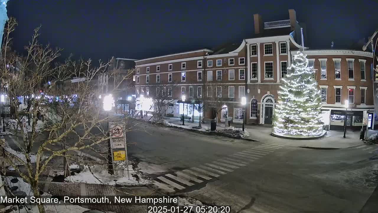 A snow-covered Market Square at night, featuring a large illuminated Christmas tree in front of brick buildings.
