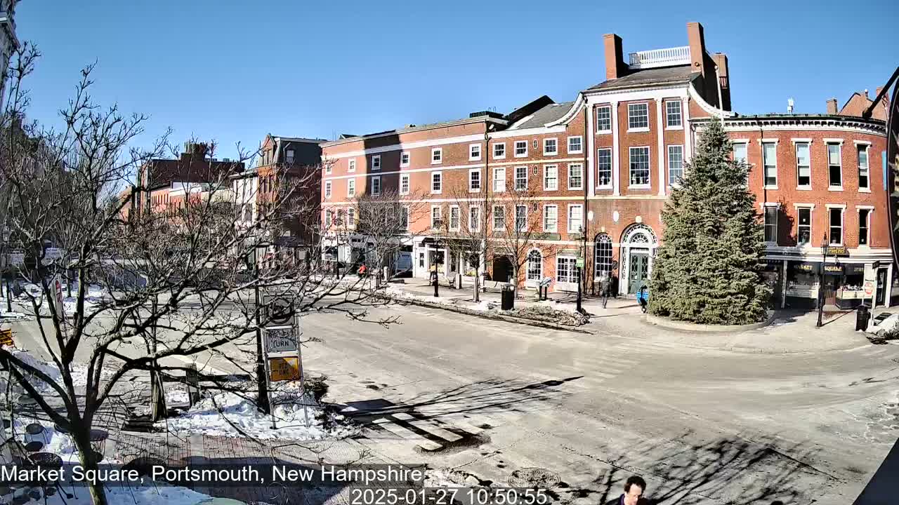 A sunny day in a brick-building-lined town square with patches of snow on the ground and bare trees.