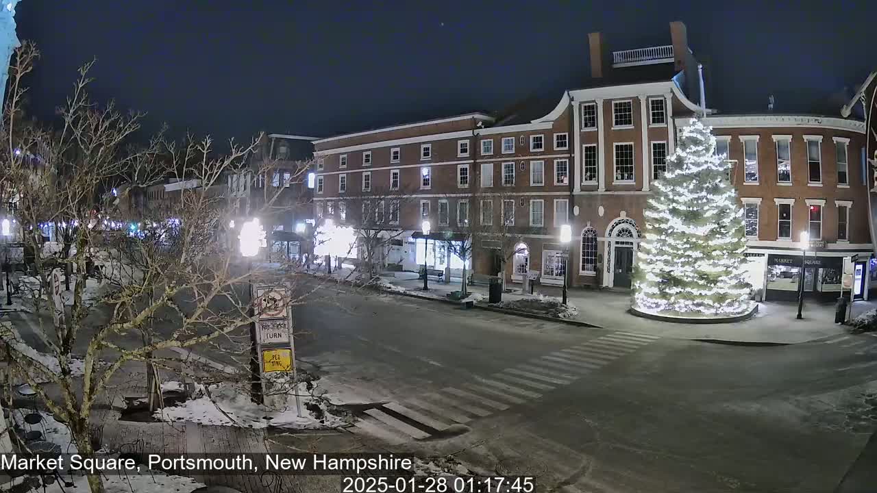 A snow-covered Market Square at night, illuminated by streetlights and a large, brightly lit Christmas tree in the center.
