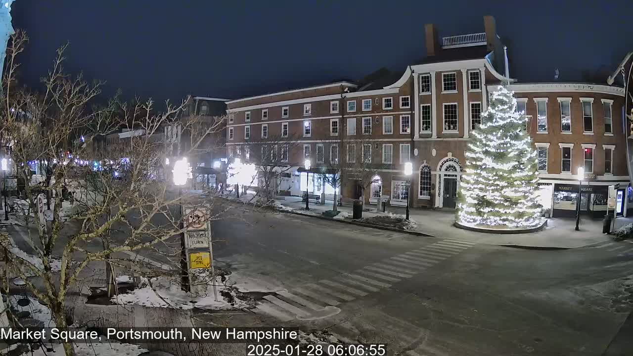 A snow-covered Market Square at night features a large, illuminated Christmas tree in front of brick buildings.
