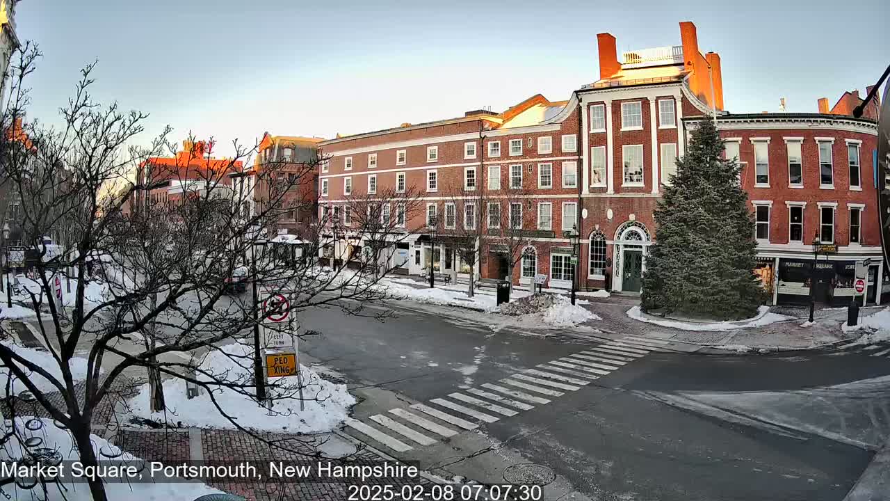 A snow-covered street scene shows a row of brick buildings under a clear, bright sky.